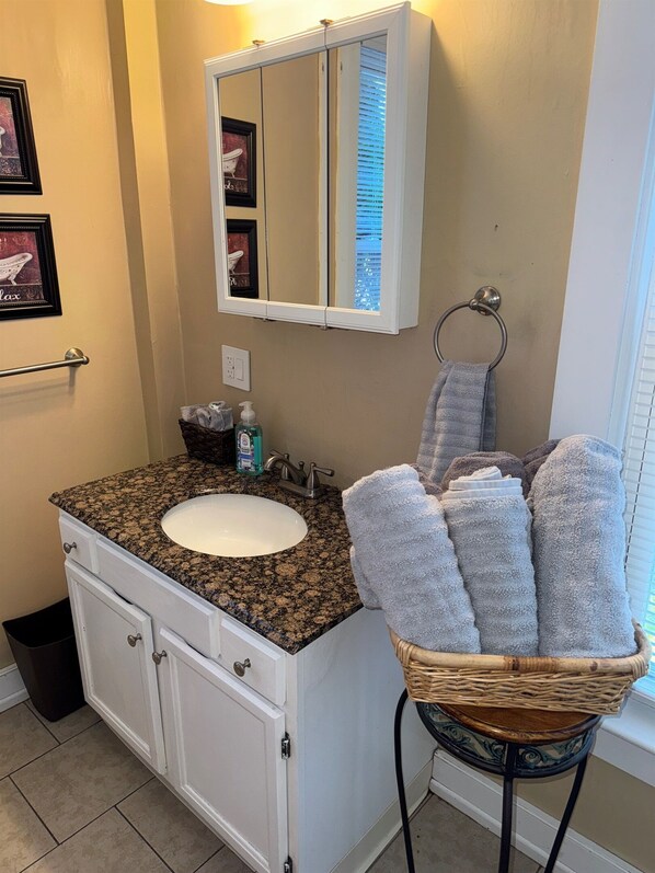 A bathroom with a granite countertop sink, white cabinets, a mirror, and a wicker basket with towels.