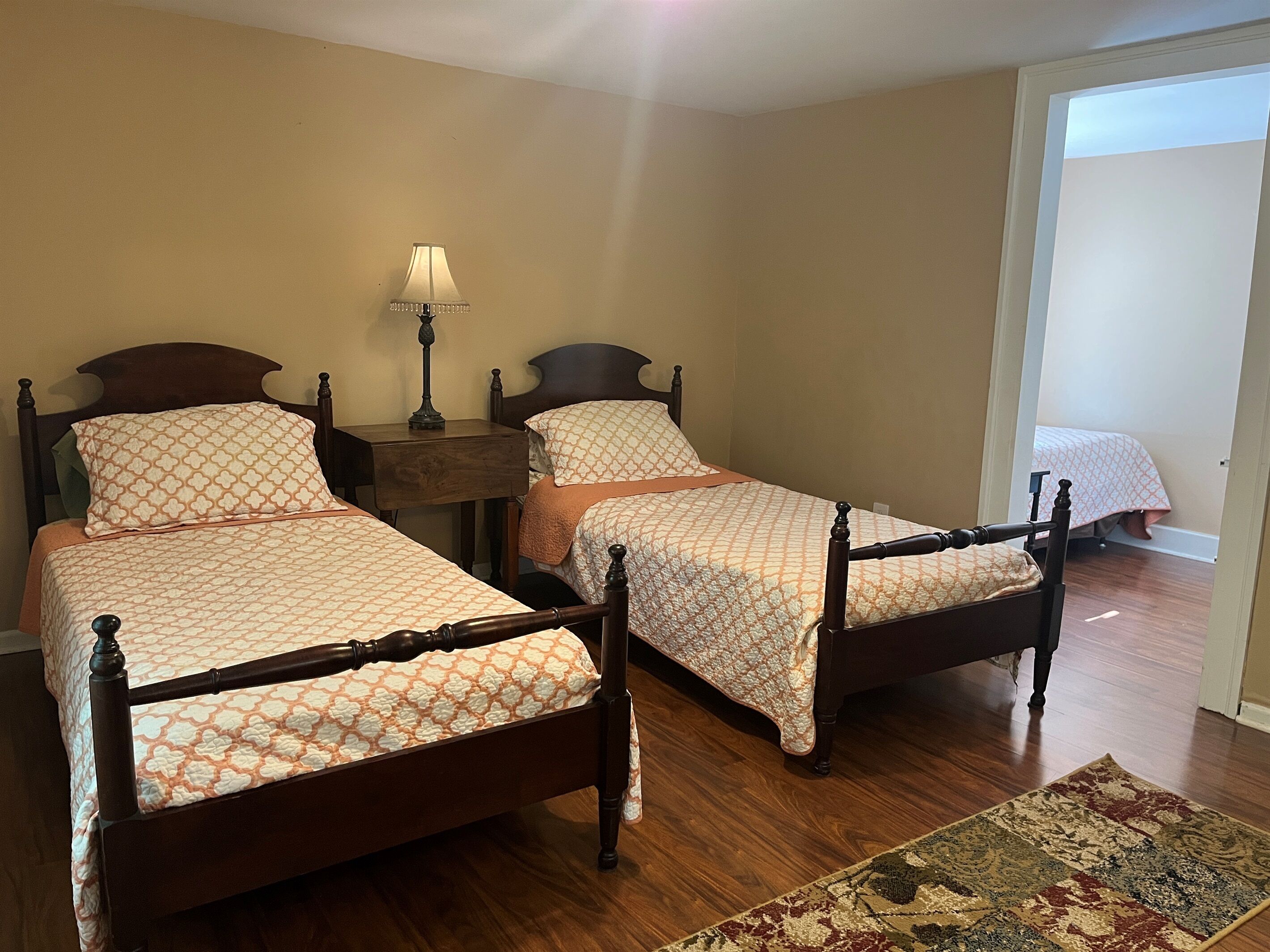 A room with two wooden beds, a nightstand with a lamp, and a wooden floor.