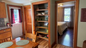 A compact kitchen with wooden cabinets, a dining table with placemats, and a built-in shelving unit with dishes and glasses.