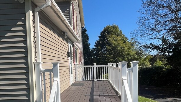 A wooden deck leading to a house with a white railing and a mailbox on the left.