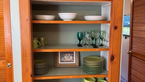 A wooden cabinet with multiple shelves containing kitchenware, a framed picture, and a red slow cooker.