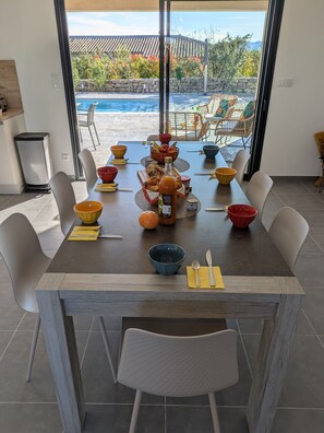 A dining table set with bowls, plates, and cutlery, overlooking a swimming pool and outdoor seating area. - New Villa Floria**** with a private heated pool in southern Ardèche (Joyeuse)