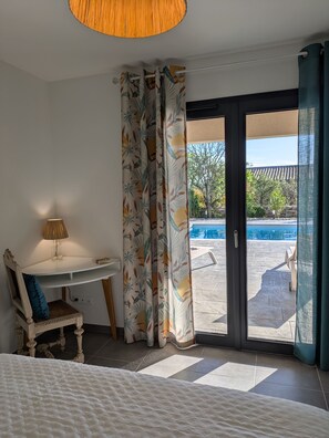 A bedroom with a bed, a desk, a chair, and a view of a swimming pool. - New Villa Floria**** with a private heated pool in southern Ardèche (Joyeuse)