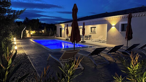 A swimming pool with lounge chairs and umbrellas, surrounded by a patio area with a stone floor and plants. - New Villa Floria**** with Private Heated Pool in South Ardèche (Joyeuse)