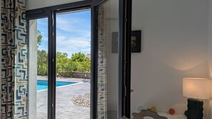 A room with a sliding glass door leading to a swimming pool area, a small table with a lamp, and a decorative birdcage. - New Villa Floria**** with Private Heated Pool in South Ardèche (Joyeuse)
