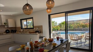 A modern kitchen with a large island, a dining area with a view of a pool, and a stone wall. - New Villa Floria**** with Private Heated Pool in South Ardèche (Joyeuse)