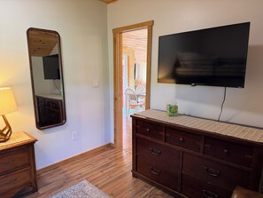 A room with a wooden dresser, a mirror, a television, and a door leading to another space. - Cozy Cabin - Quaint cabin, with great view and firepit (Milford)