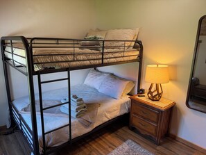 A bunk bed with a bedside table and lamp, a mirror, and a patterned rug.