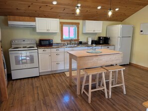 A kitchen with wooden flooring, white cabinetry, a central island with stools, and a ceiling with exposed beams and pendant lights.