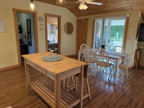 A wooden dining table with chairs, a ceiling fan, and a view of the outdoors through a window.