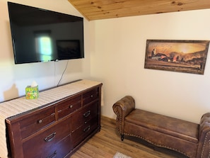Una habitación con techo de madera, un televisor de pantalla plana montado en la pared, un sofá de cuero marrón, un aparador de madera con cajones y un cuadro enmarcado en la pared.