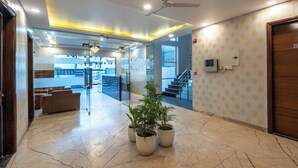 A lobby with a marble floor, potted plants, a ceiling fan, and a staircase in the background. - Saavi Hotel Sector- 46 (Gurugram)