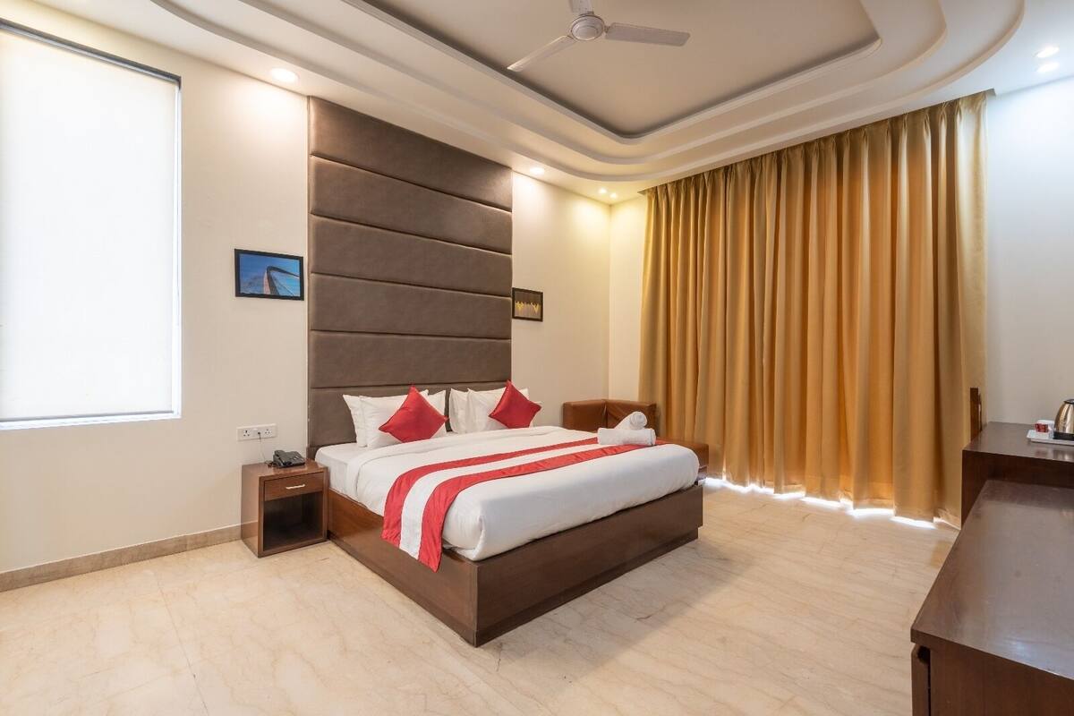 A modern hotel room with a large bed, a nightstand, a desk, and a window with curtains.