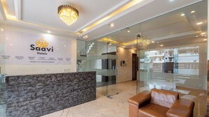 A modern hotel lobby with a reception desk, a chandelier, and a leather sofa. - Saavi Hotel Sector- 46 (Gurugram)