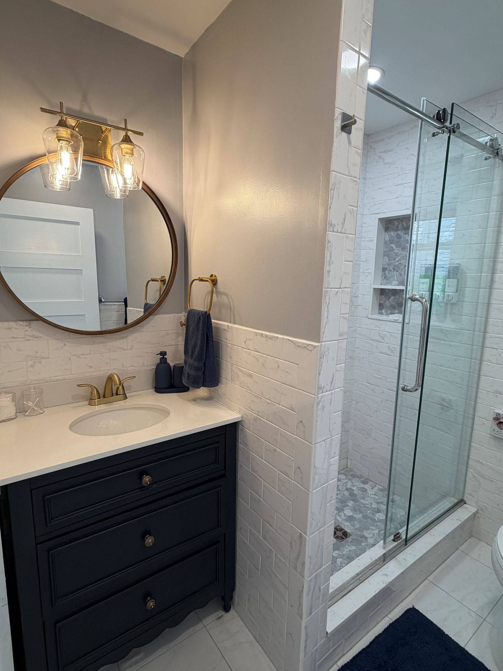 A modern bathroom with a round mirror, a sink, a vanity with drawers, and a glass shower enclosure.