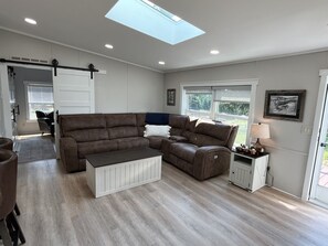 A living room with a brown sectional sofa, a white coffee table, a lamp, and a view of the outdoors through a window. - Fountain View - Recent reno, Farmhouse Chic! (Milford)