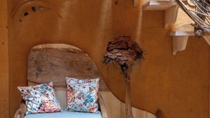 A rustic wooden chair with a cushion, a decorative branch, and a wall with a textured finish. - Gaia" Hobbit House (Vittel)