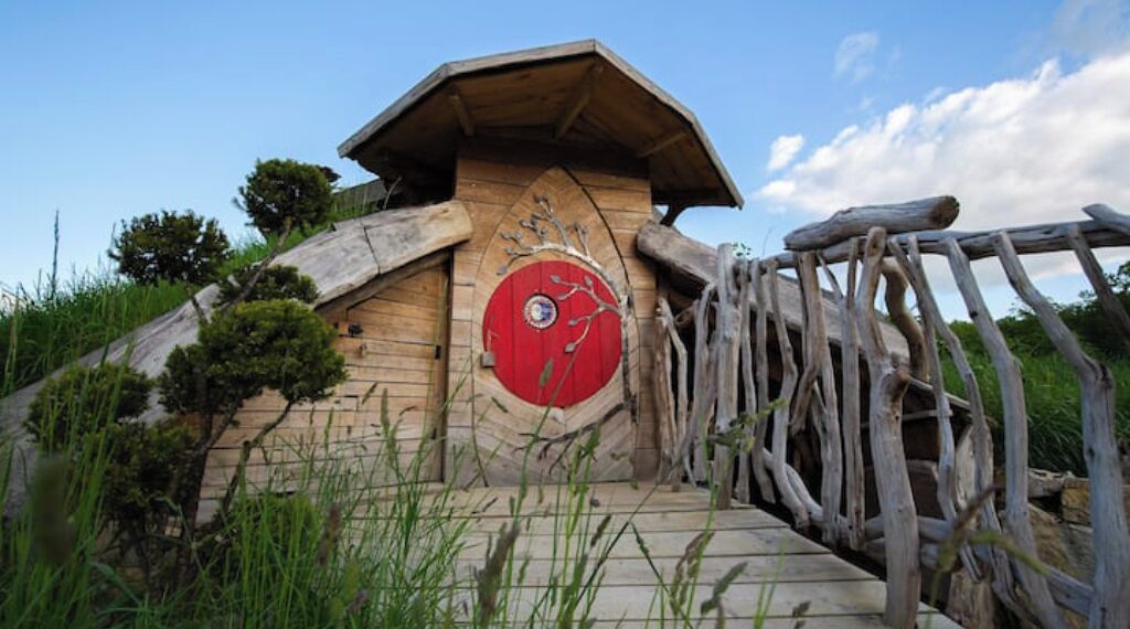 A wooden structure with a red circular door, a wooden roof, and a wooden fence.