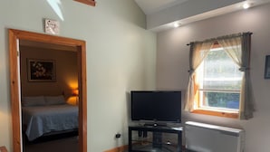 Una habitación con cama, televisor sobre un mueble, radiador y ventana con cortinas.