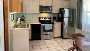 Una cocina compacta con armarios blancos, un refrigerador de acero inoxidable, un microondas, un horno y un lavavajillas.