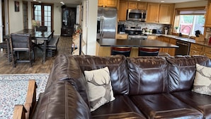 A modern kitchen with stainless steel appliances, wooden cabinets, and a dining area with a leather couch and chairs.