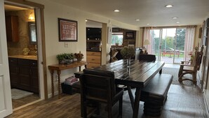 A spacious dining area with a long wooden table and benches, a kitchen with dark cabinets, and a stone fireplace.