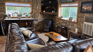 A cozy living room with a stone wall, leather sofa, wooden coffee table, and a fireplace.