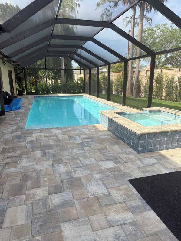 A covered swimming pool with a tiled deck, a separate hot tub area, and a view of the surrounding greenery.