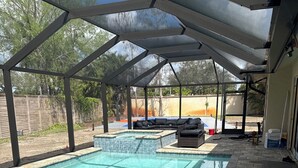 A covered swimming pool with a tiled edge, a lounge area with a sofa, and a brick patio. - Mini Resort , 3 BR newly renovated, Gym , pool , spa , pickleball,basketball (Naples)