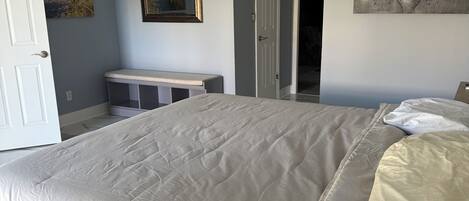 Un dormitorio con una cama grande, un ventilador de techo, un escritorio y una puerta que da a otra habitación.