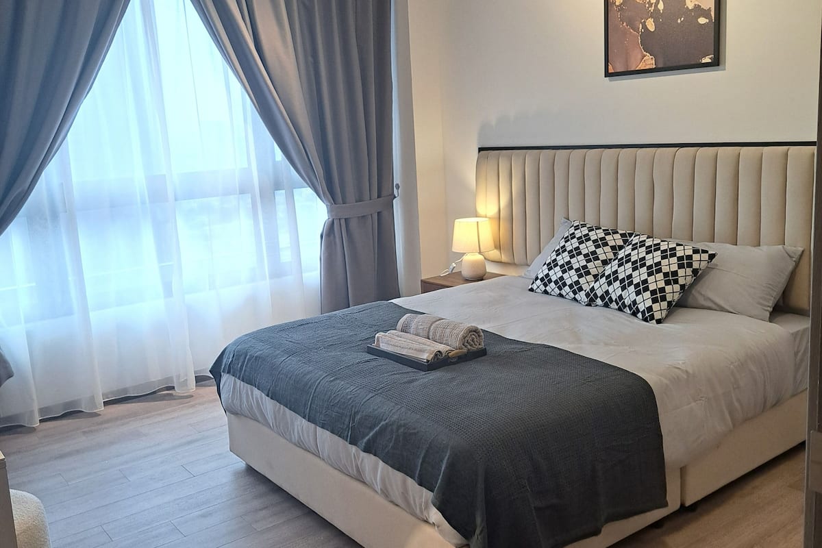 A modern bedroom with a large bed, a headboard, a bedside table with a lamp, and a wall-mounted artwork.