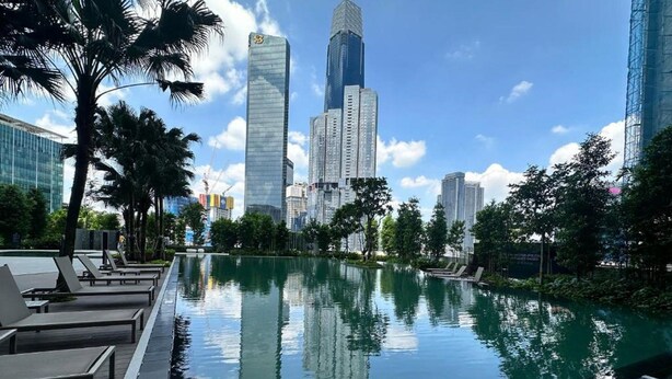 A pool with lounge chairs, surrounded by tall buildings and palm trees. - AGILE Service Residence by Sha (Kuala Lumpur)