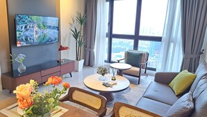 A modern living room with a flat-screen TV, a sofa, a coffee table, and a dining table with flowers. - AGILE Service Residence by Sha (Kuala Lumpur)