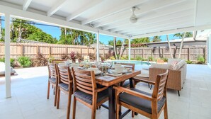 Un patio techado con una mesa de comedor dispuesta para cuatro personas, rodeado de sillas de madera con cojines.