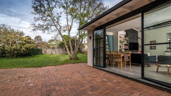 A modern house with a brick patio, large sliding glass doors leading to a dining area with wooden furniture.