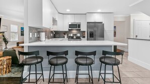Een moderne keuken met een groot eiland, barkrukken, roestvrijstalen apparatuur en een neutraal kleurenpalet.