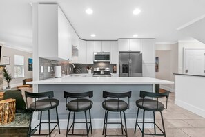 A modern kitchen with a large island, bar stools, stainless steel appliances, and a neutral color palette.
