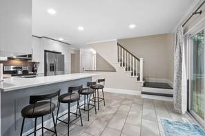 A modern kitchen with a central island, bar stools, and a staircase leading to a balcony.