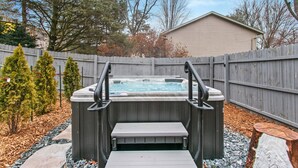 Een hottub met treden, omgeven door een houten hek, bomen en een tuinhuis in een achtertuin.
