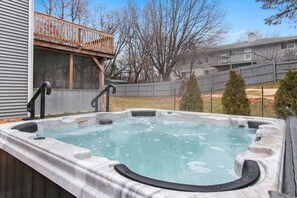 Un bain à remous avec une terrasse en bois, une clôture en bois et une maison en arrière-plan.