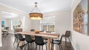 Een eetgedeelte met een grote houten tafel, zwarte stoelen, een hangende koperen lamp en uitzicht op een waterval door een raam.