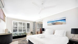 Un dormitorio con cama, ventilador de techo, un cuadro y una ventana con persianas.