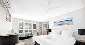 Une chambre à coucher avec un lit, un ventilateur de plafond, un tableau et une fenêtre avec des stores.
