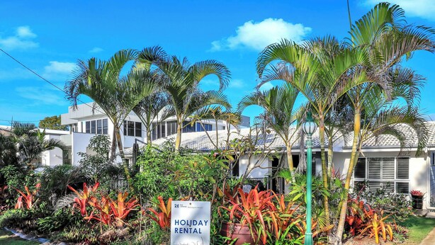 Un edificio moderno con un cartel que indica 'Holiday Rental' y exuberante vegetación tropical al frente.
