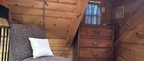 Une pièce chaleureuse aménagée comme une cabane, avec un fauteuil à motifs, une commode en bois et un petit tapis.