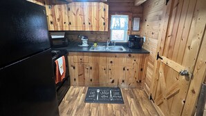 A wooden cabin kitchen with a black refrigerator, a microwave, a coffee maker, and a sink. - Cozy log cabin located in downtown Moravia, Iowa.  (Moravia)