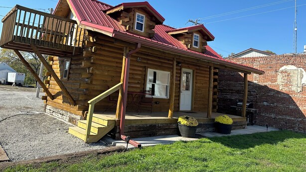 A wooden log cabin with a red roof, a porch, and a small balcony. - Cozy log cabin located in downtown Moravia, Iowa.  (Moravia)