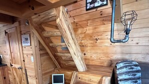 A wooden cabin interior with a loft bedroom, a desk with a laptop, a bed, and a rustic light fixture. - Cozy log cabin located in downtown Moravia, Iowa.  (Moravia)