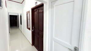 A hallway with a white door on the right, a brown door with a window on the left, and a number sign above the brown door. - Semarang Inn (Semarang)