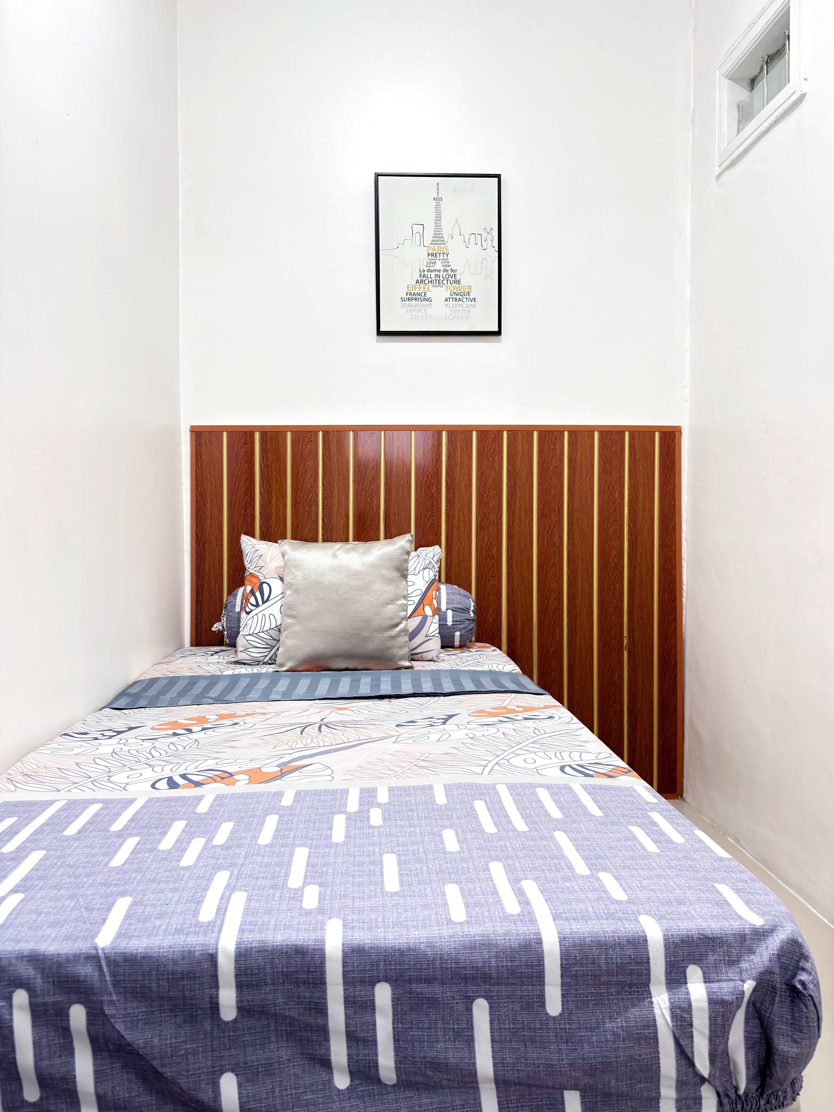 Un dormitorio con cabecera de madera, una cama con ropa de cama estampada y un cuadro en la pared.